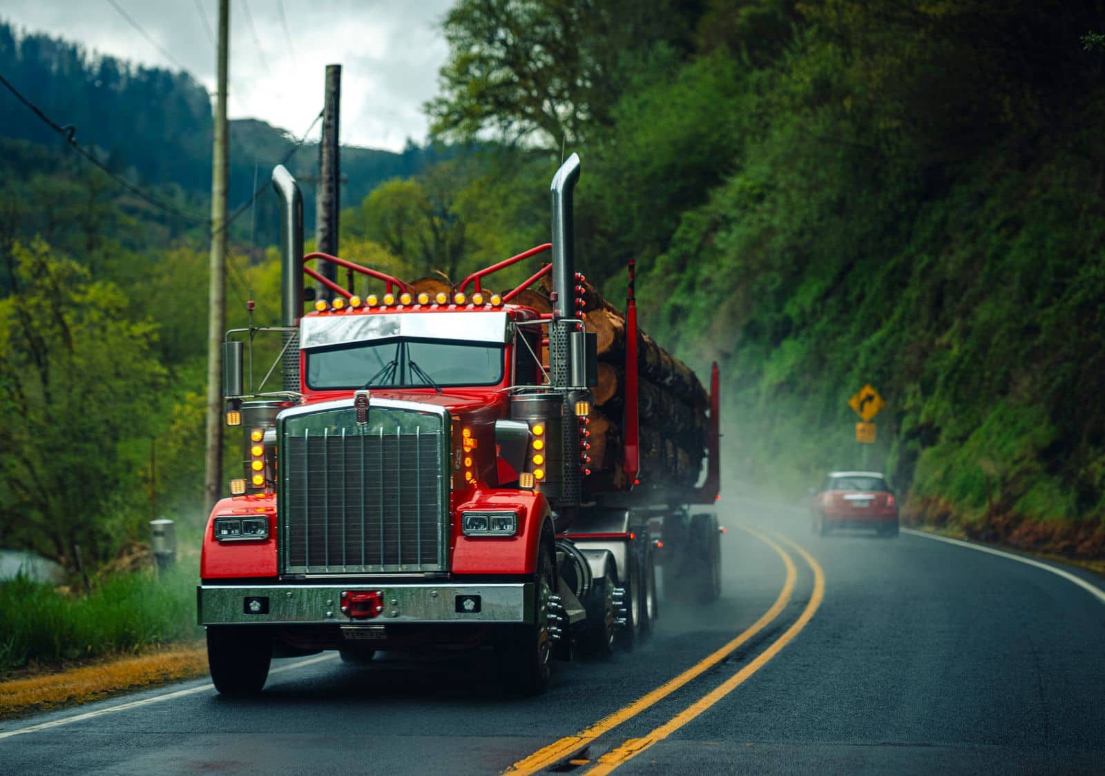 A loaded log truck rolling down a wet two lane Oregon highway